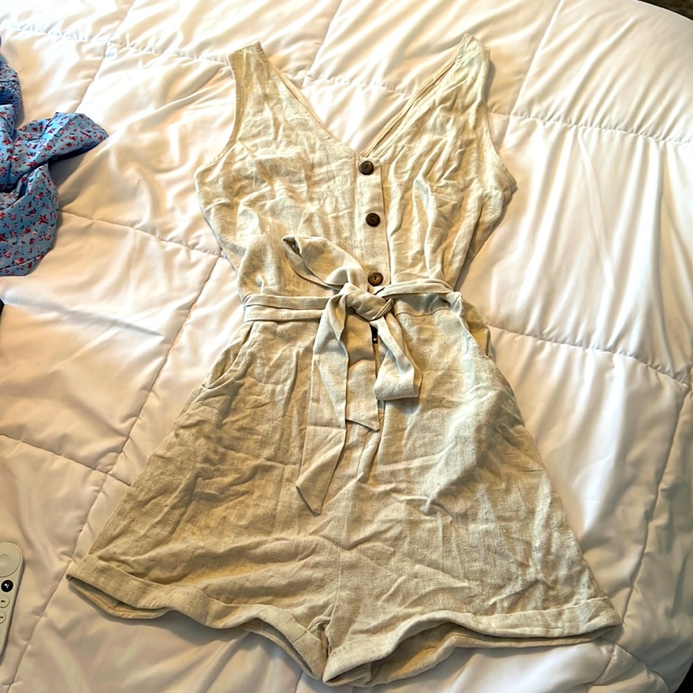 Tan romper with waist tie, pockets, and accent buttons.